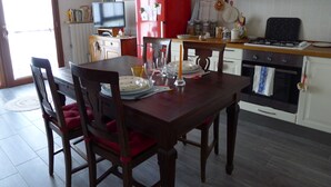 Ein Essbereich mit einem Holztisch, gedeckt für vier Personen, umgeben von Stühlen. Im Hintergrund sind ein roter Kühlschrank und ein Herd zu sehen.