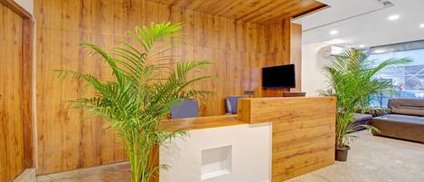 Un espace d’accueil avec un comptoir de réception en bois, un téléviseur à écran plat et des plantes en pot.