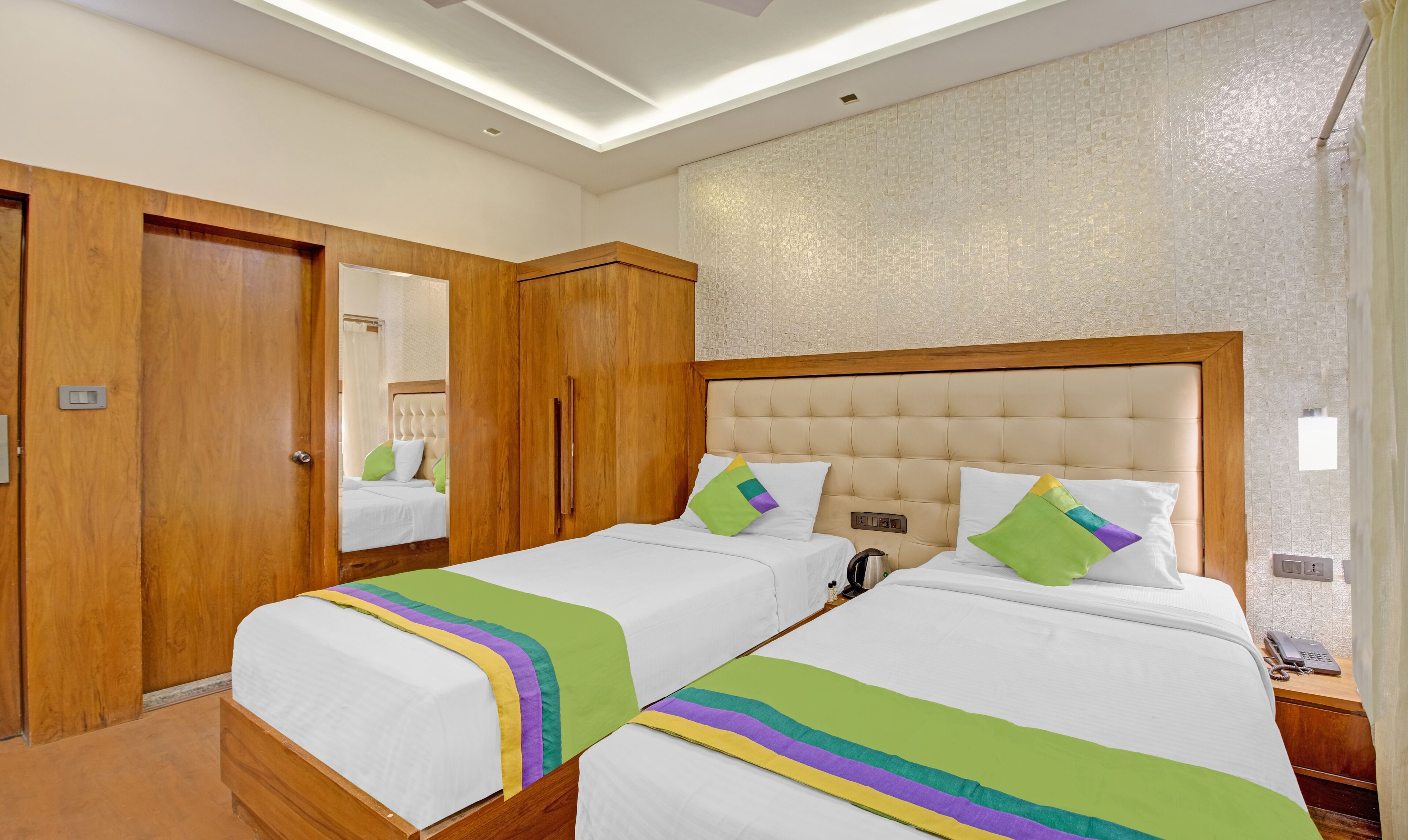 A hotel room with two beds, wooden wardrobe, and a mirror.