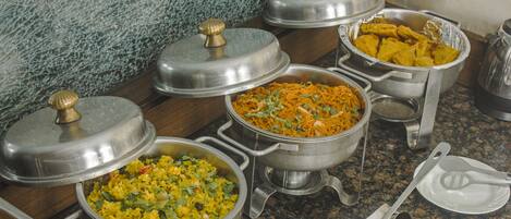 A buffet setup with various dishes in metal serving containers, some with lids.