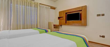 Una habitación de hotel con dos camas, un televisor montado en la pared, una silla y un equipo de aire acondicionado.