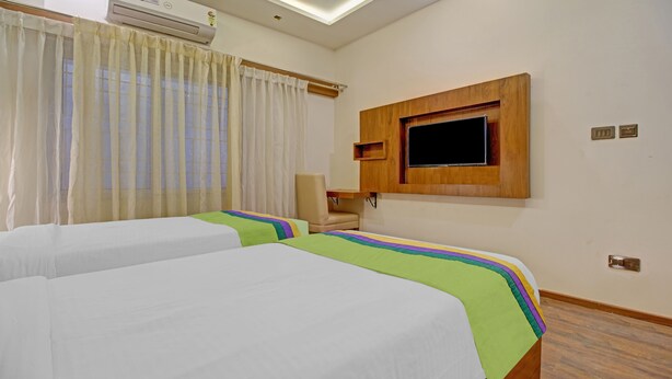 A hotel room with two beds, a TV mounted on the wall, a chair, and an air conditioning unit.