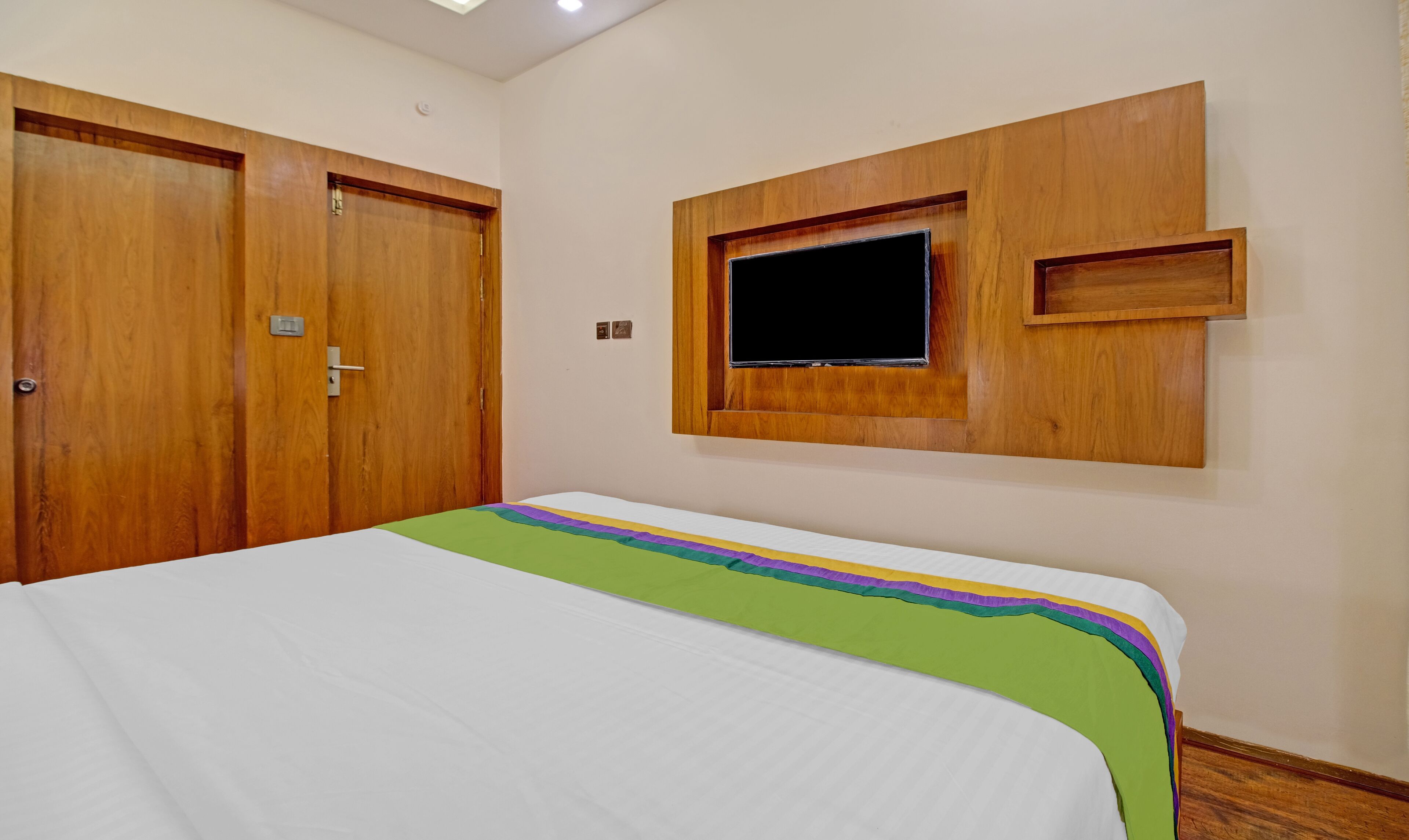 Une chambre d’hôtel avec un lit, une armoire en bois et un téléviseur fixé au mur.