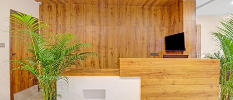 A reception area with a wooden wall, a flat-screen TV, and potted plants.