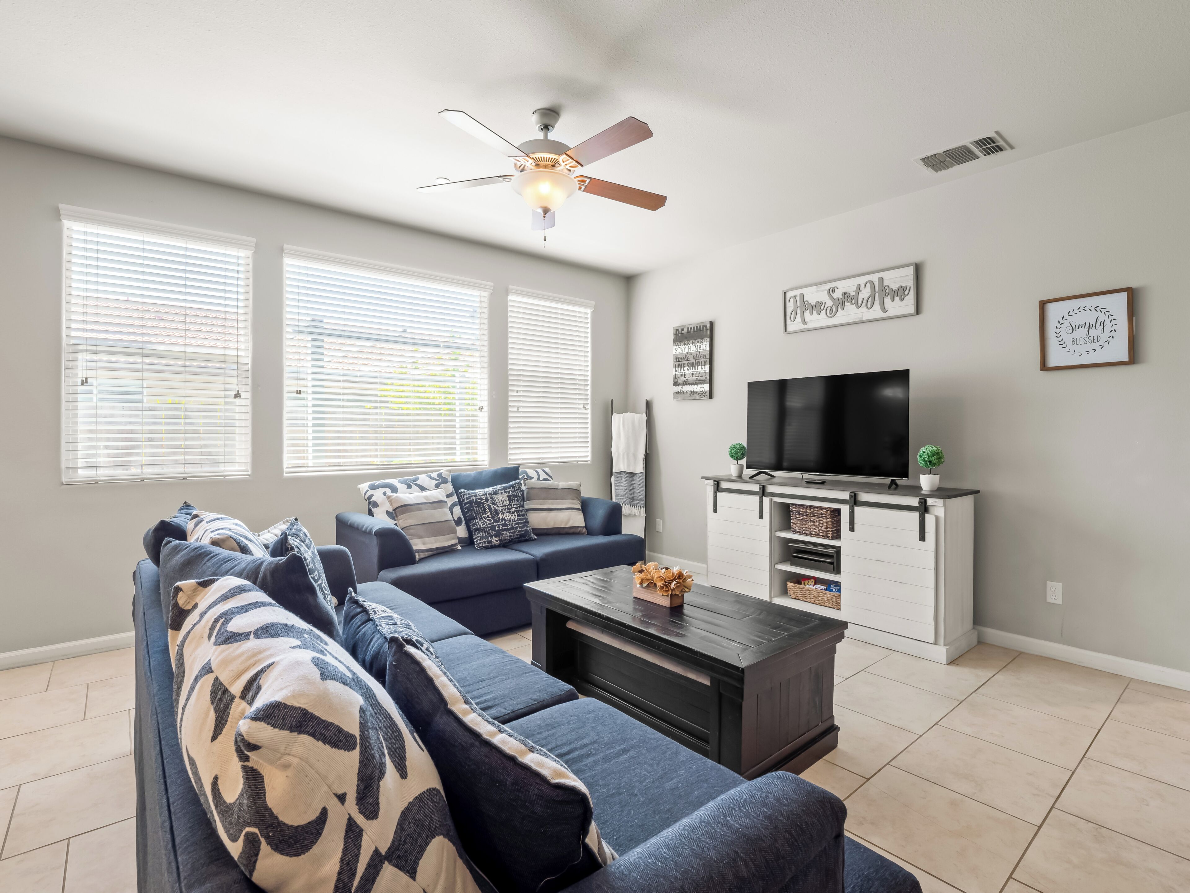 A living room with a sectional sofa, a coffee table, a TV, and a ceiling fan.