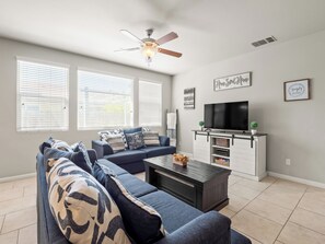 A living room with a sectional sofa, a coffee table, a TV, and a ceiling fan.