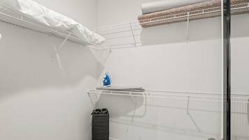 Een kamer met een stapelbed, een klein strijkplank en een prullenbak.