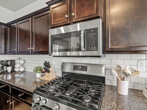 A kitchen with dark wood cabinets, a stainless steel microwave, a gas stove, and a coffee maker.