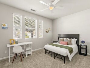 A bedroom with a bed, desk, chair, and a ceiling fan.