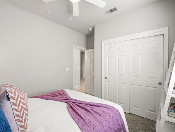 A bedroom with a bed, a door, and a white ceiling fan.
