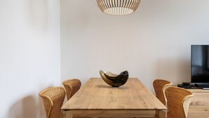 Un comedor con una mesa de madera, un original centro de mesa en un cuenco, sillas de mimbre y un televisor sobre un mueble de madera.