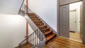 Una escalera de caracol con escalones de madera y barandillas de metal, que conduce a una puerta con picaporte blanco.