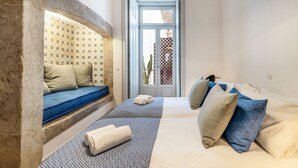 Una habitación con una cama, un banco con cojines y un papel tapiz estampado.