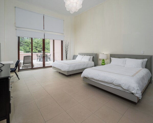 A hotel room with two beds, a desk, and a chair. There is a sliding glass door leading to an outdoor area with a table and chairs. - Spacious 1BR Loft - Plaza Buenaventura Resort (Río Hato)