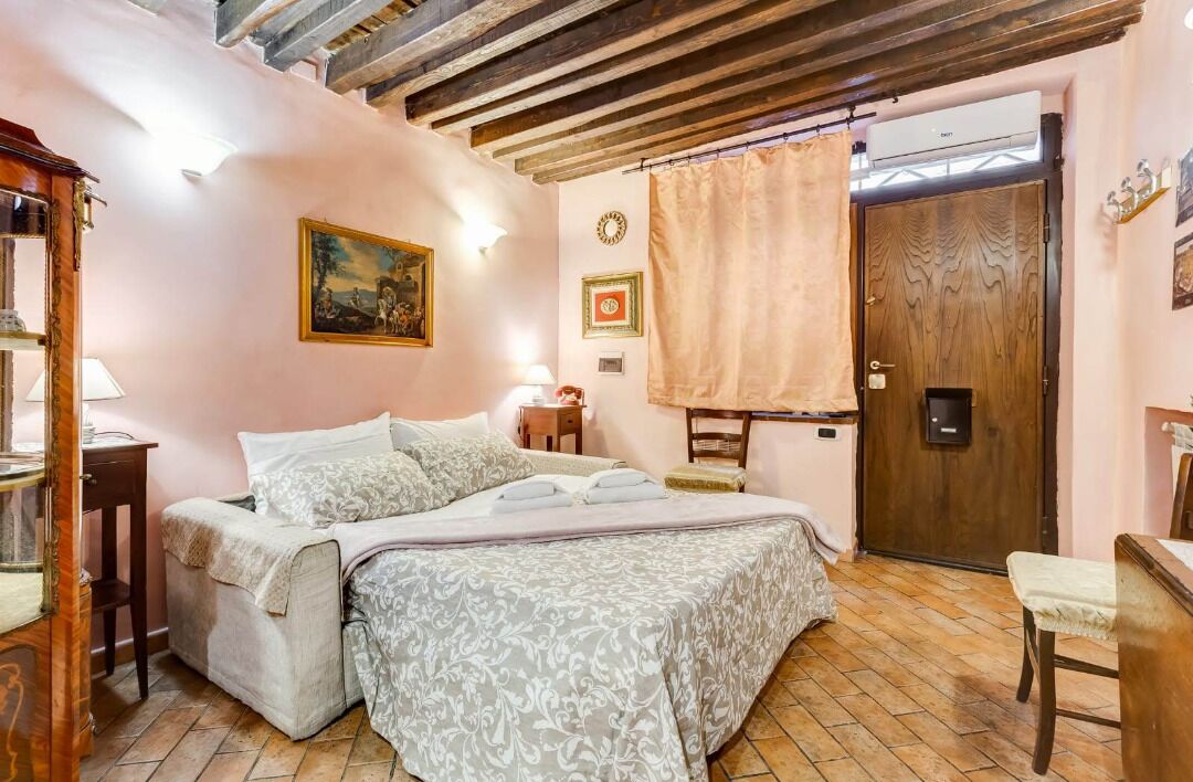 A bedroom with a bed, a wooden door, a small table, and a chair.