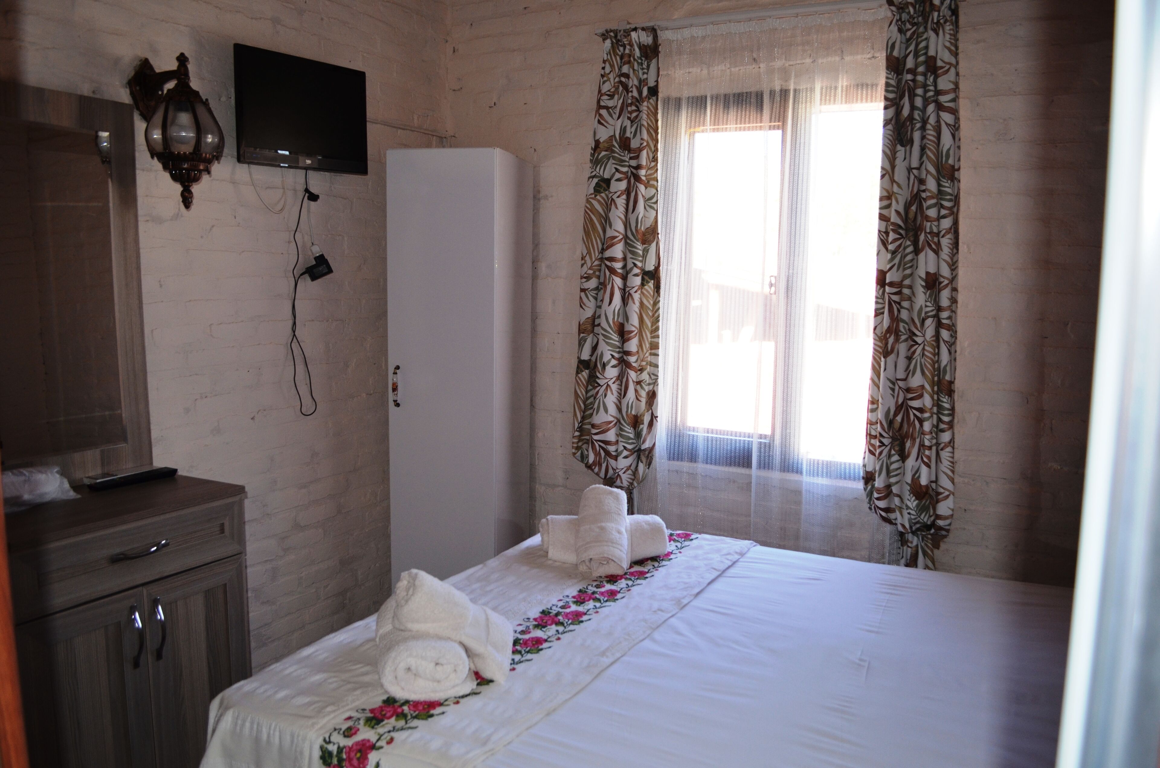 A hotel room with a bed, a TV mounted on the wall, a wardrobe, and a window with curtains.