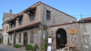 A stone building with a tiled roof, a wooden door, and a small outdoor seating area with a table and chairs. - Nezisin Konagi (Ayvalik)