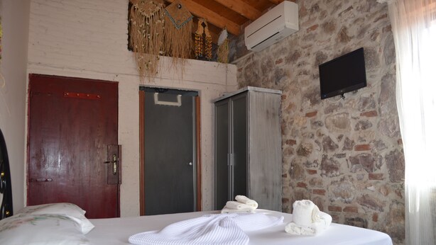 A bedroom with a bed, a wardrobe, and a television on a stone wall. - Nezisin Konagi (Ayvalik)