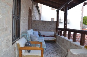 A covered outdoor seating area with a sofa and chairs, a patterned floor, and a brick wall. - Nezisin Konagi (Ayvalik)