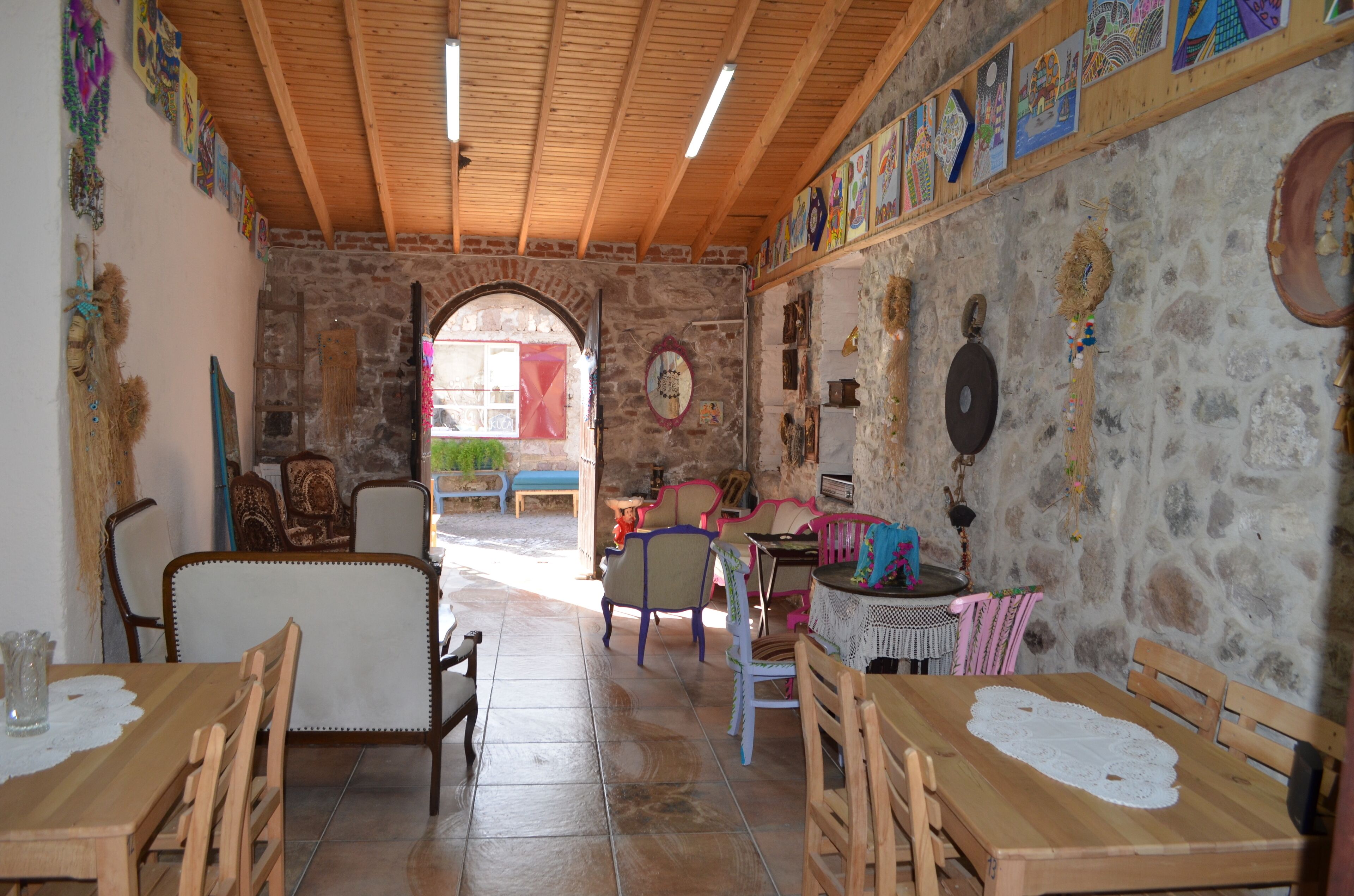A rustic dining area with wooden tables and chairs, stone walls, and colorful artwork.