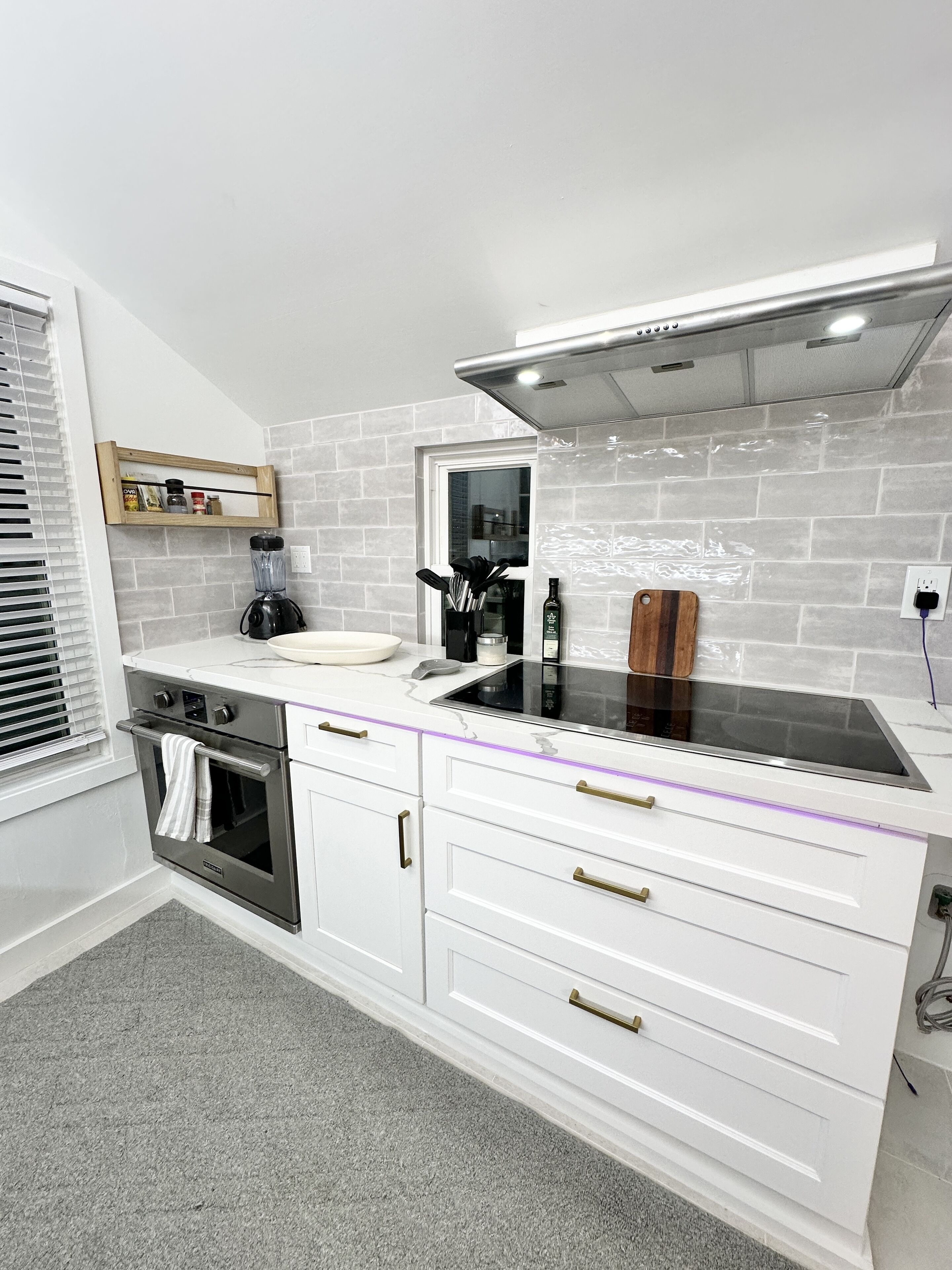 Een moderne keuken met witte kastjes, een ingebouwde oven, een roestvrijstalen afzuigkap en een aanrecht met een blender en andere apparaten.