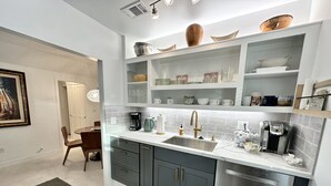 Una cocina moderna con armarios grises, un lavavajillas de acero inoxidable y una cafetera. Hay estantes sobre la encimera con varios utensilios de cocina.