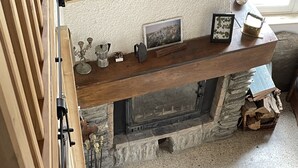 Eine Treppe führt zu einem Wohnbereich mit Kamin aus Stein, Holzregalen und Blick ins Innere.