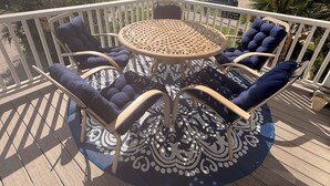 Een overdekt terras buiten, met een ronde tafel en stoelen, omringd door een witte balustrade.