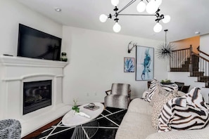 Un salon moderne avec une cheminée, un téléviseur, un fauteuil à motifs et un escalier.