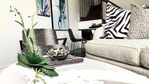 A living room with a white coffee table, a sofa, and a chair. There are books and a decorative bowl on the table. - Comfortable Chic | Long Term | Legacy (Plano)