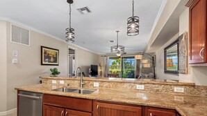 A kitchen with granite countertops, wooden cabinets, stainless steel appliances, pendant lighting, and a view of the outdoors.