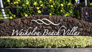 A sign for Waikoloa Beach Villas with a landscaped area in the background.