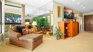 A living room with a wicker sofa, a wooden entertainment center, and a large window with a view of trees. - Includes Beach Gear! Spacious lanai with resort views.  #2 Shores at Waikoloa (Waikoloa Beach Resort)
