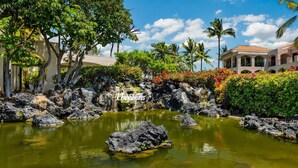 A tropical garden with a koi pond, palm trees, and a building with a tiled roof. - Includes Beach Gear! Spacious lanai with resort views.  #2 Shores at Waikoloa (Waikoloa Beach Resort)