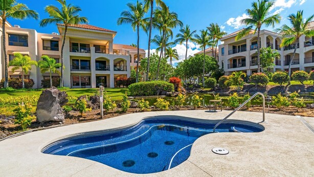A swimming pool with a curved edge, surrounded by a concrete deck. There are palm trees and a landscaped garden with various plants and a small pond. - Includes Beach Gear! Spacious lanai with resort views.  #2 Shores at Waikoloa (Waikoloa Beach Resort)