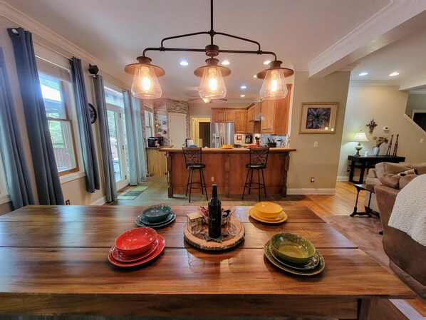 A dining area with a wooden table, bar stools, and a kitchen in the background.