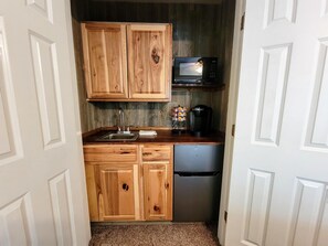 A compact kitchen with wooden cabinets, a stainless steel sink, a microwave, and a coffee maker.