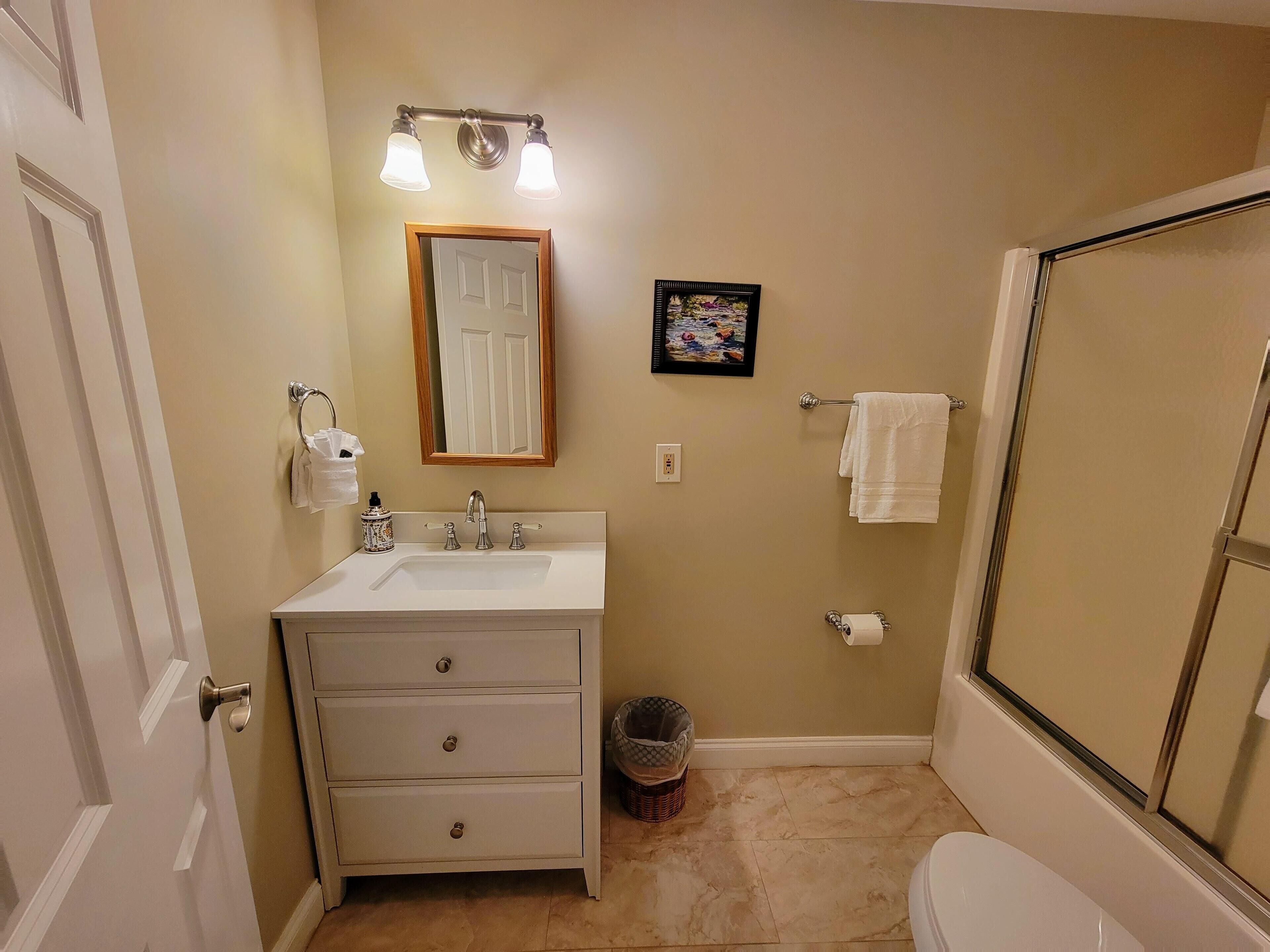 A bathroom with a sink, mirror, towel rack, and shower.