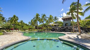 A swimming pool with a curved design, surrounded by palm trees and a small pavilion.