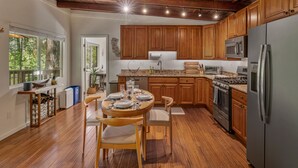 Une cuisine avec des meubles en bois, un réfrigérateur en acier inoxydable, un four à micro-ondes et une cuisinière. On y trouve une table à manger avec des chaises et une fenêtre avec des stores.