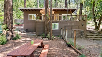 Une cabane dotée d’une terrasse, entourée d’arbres et agrémentée d’une table de pique-nique.