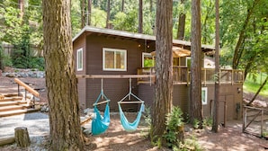 Une cabane dotée d’une terrasse et d’un hamac, entourée d’arbres.