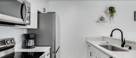 Une cuisine moderne dotée d’appareils électroménagers en acier inoxydable, d’un plan de travail blanc et d’un parquet en bois.