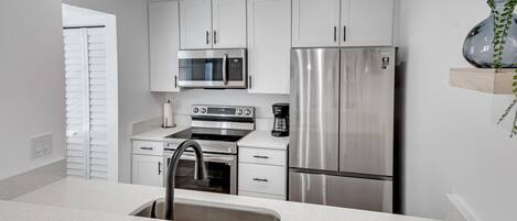 A modern kitchen with white cabinetry, stainless steel appliances, and a built-in sink.