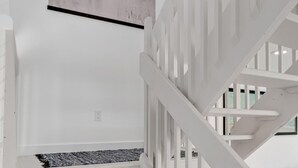 A white staircase with a handrail, a black and white artwork on the wall, and a gray sofa in the background. - Beachside Duplex A (Saint Augustine Beach)