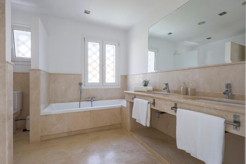 Ein modernes Badezimmer mit einer großen Badewanne, zwei Waschbecken, einem Spiegel und einem Fenster.
