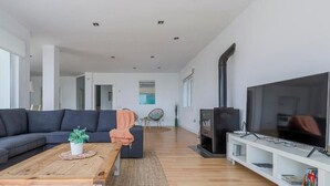 Ein modernes Wohnzimmer mit großem Fernseher, dunklem Sofa, Couchtisch aus Holz und einer TV-Konsole mit Regalen.