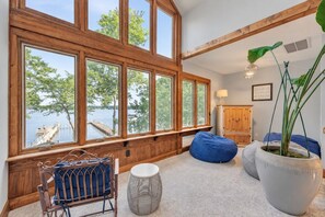 A room with large windows overlooking a body of water, a wooden cabinet, a blue bean bag, and a potted plant.