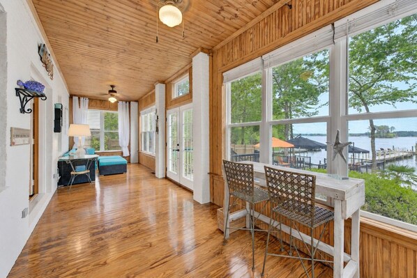A spacious room with wooden floors, large windows, and a view of a dock and water.
