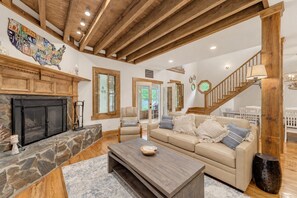 A spacious living room with a stone fireplace, a wooden ceiling, a staircase, and a large wall map.